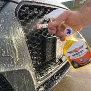 Person using a spray bottle labeled 'Bugger Off' on a car's grille.