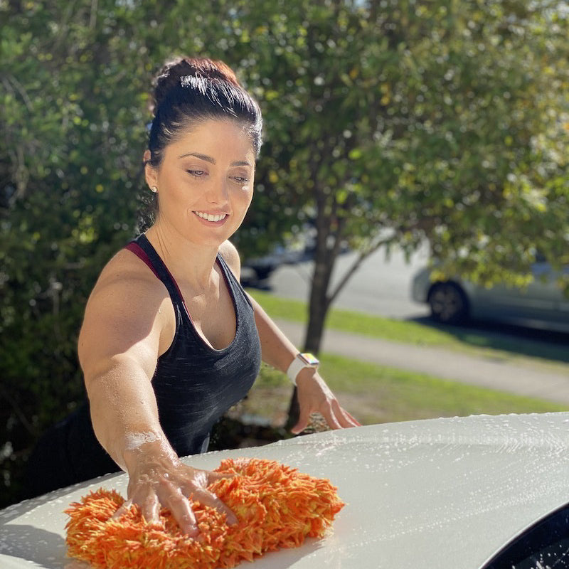 Woman washing a car with a sponge outdoors