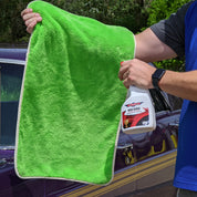 Person holding a green towel and a bottle of car care product in front of a car.