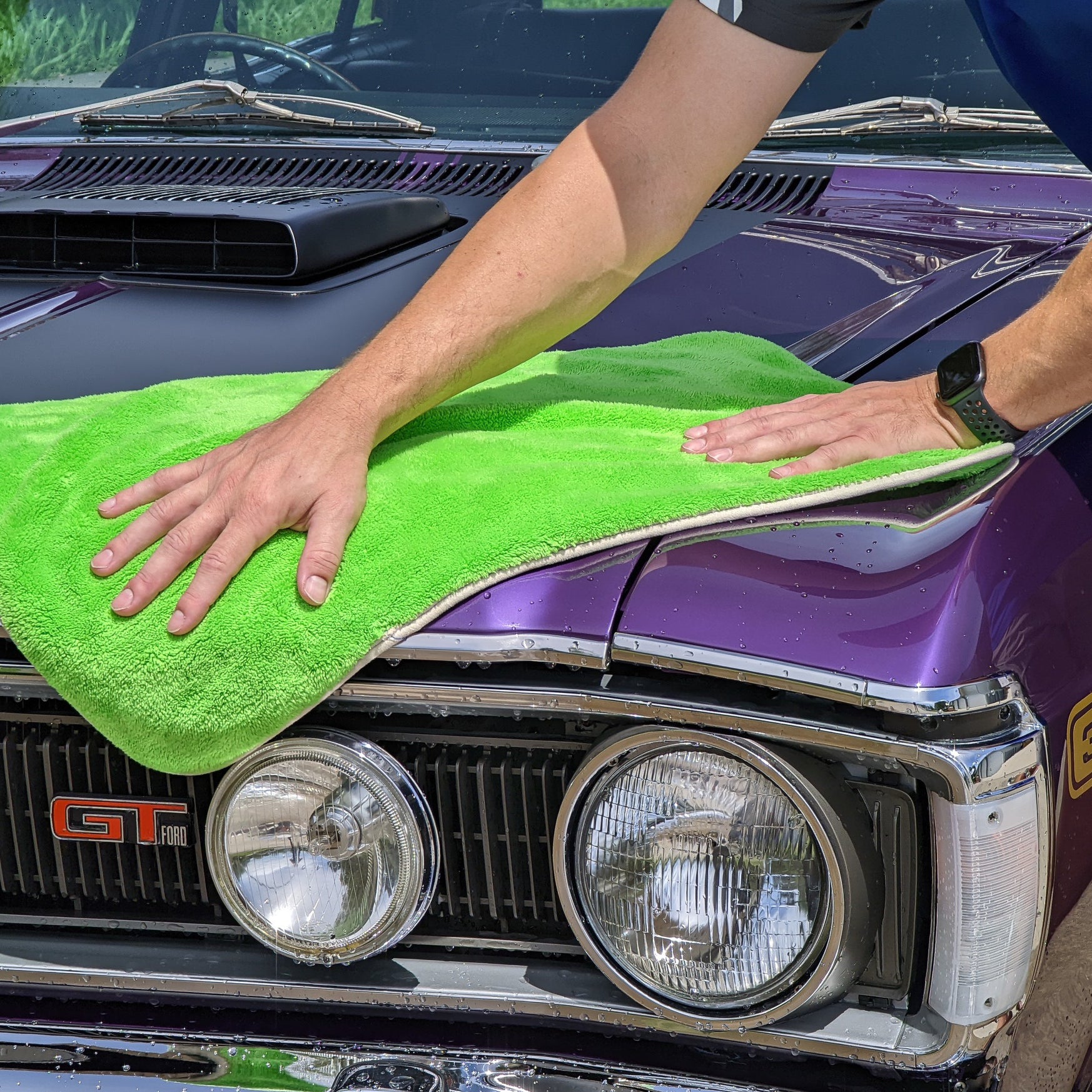 Person cleaning a classic car with a green towel
